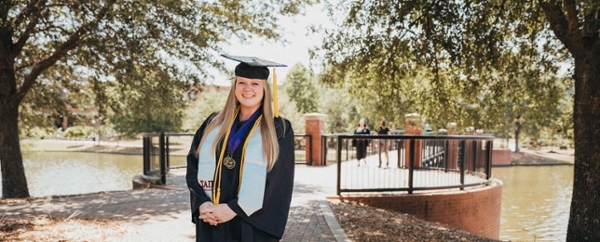 Rebecca Symone Caldwell, President’s Scholar for MGA's Class of 2022, in her cap and gown at her graduation ceremony standing by the bridge on the Macon Campus.